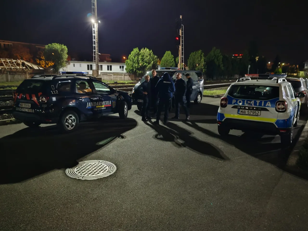Éjszakai jelenet vasúti terület közelében: csendőrségi és rendőrségi terepjárók parkolnak, közöttük egyenruhás rendőrök és csendőrök állnak csoportban egy megbeszélésen.