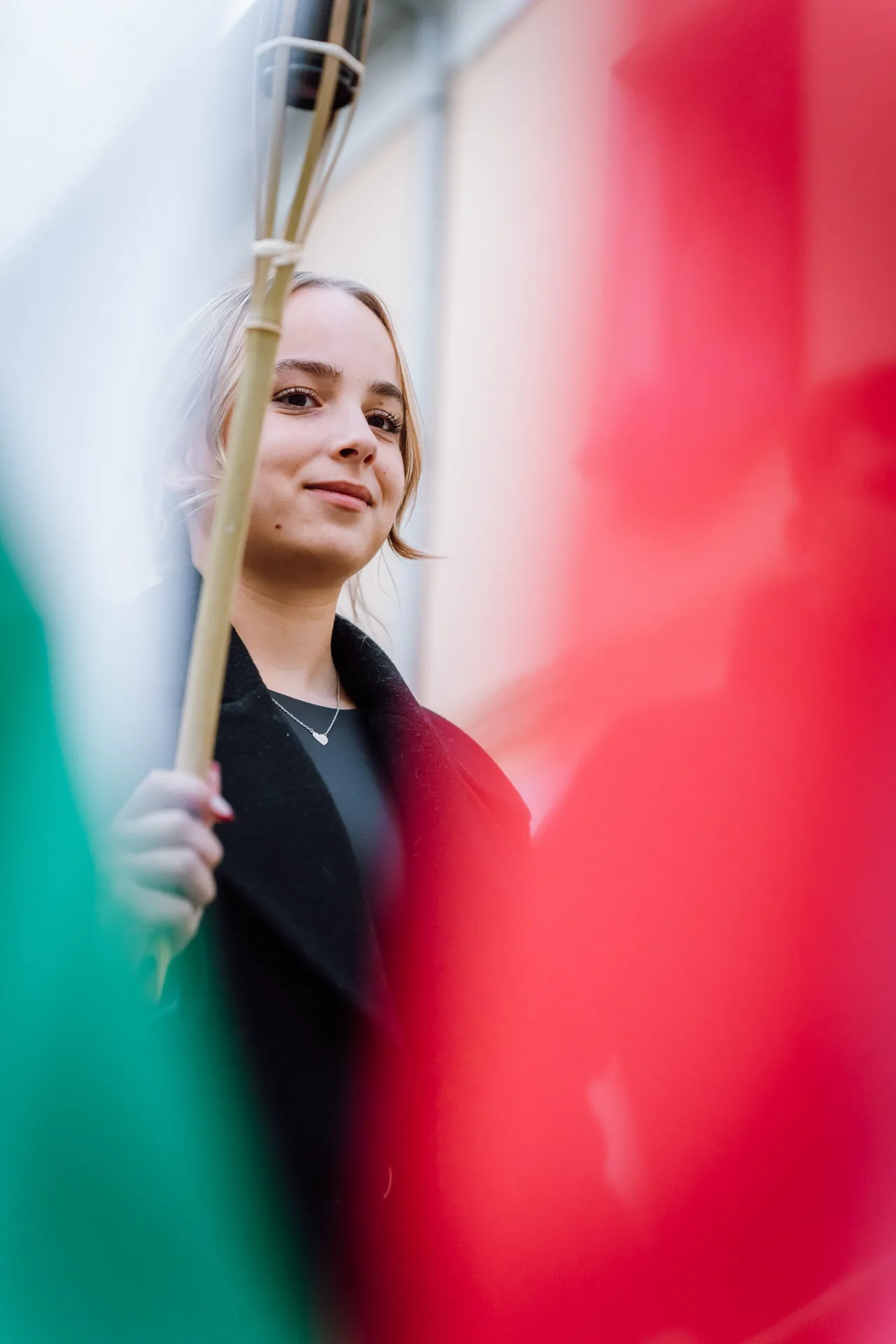 Fiatal nő portréja, előtérben elmosódó piros-fehér-zöld színű zászlók (feltehetően olasz vagy más trikolór) között, aki egy zászlórudat tart a kezében.