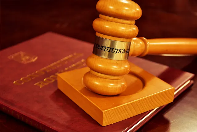 Fából készült bírói kalapács, melyre „CONSTITUȚIONALĂ” felirat van rögzítve, egy Románia Alkotmányát tartalmazó, bordó borítós könyvön fekszik.