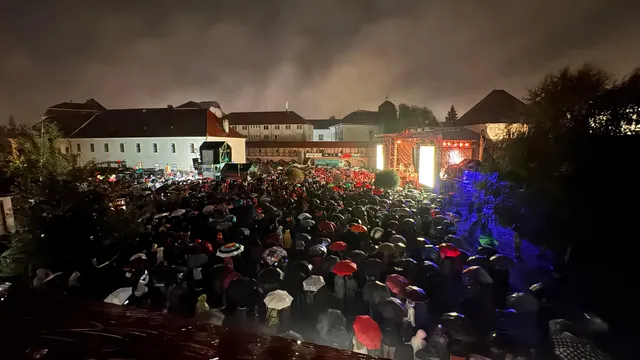 Éjszakai szabadtéri koncert a Vártéren, esőben, sok esernyős néző gyűlt össze a megvilágított színpad előtt, háttérben a vár épületei.