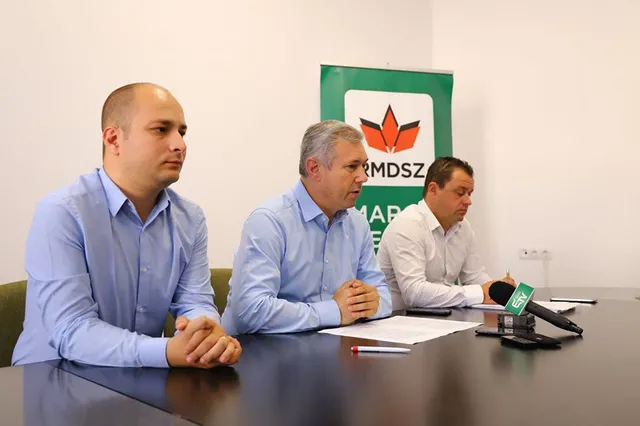Három férfi ül egy asztalnál sajtótájékoztatón, mögöttük RMDSZ Maros megyei feliratú zöld molinó látható, az asztalon mikrofonok és papírok vannak.