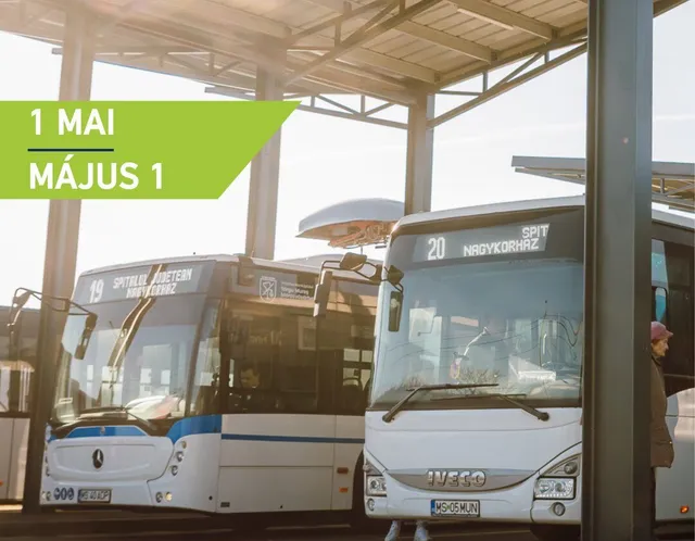 Egy fedett buszmegállóban két helyi busz áll egymás mellett, az egyiken 19-es, a másikon 20-as jelzés és úticél látható; a háttérben egy utas száll fel a jobb oldali buszra.