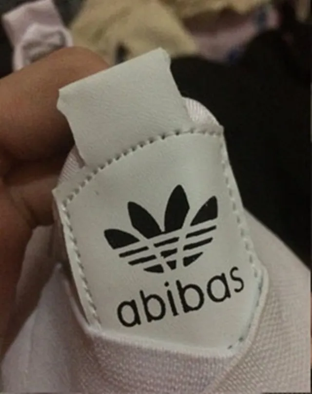 Közelkép egy cipő nyelvéről, amelyen az Adidas márka logójához hasonló háromcsíkos jelvény és „abibas” felirat látható, ami a márka hamisítványára utal.