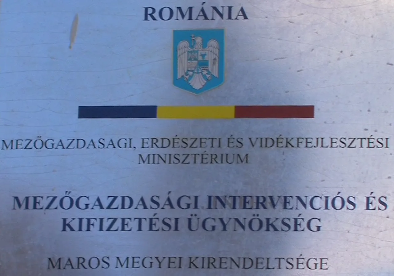 Fémtábla felirata: „ROMÁNIA” felirat és címer felett, alatta „Mezőgazdasági, Erdészeti és Vidékfejlesztési Minisztérium”, majd „Mezőgazdasági Intervenciós és Kifizetési Ügynökség”, alul „Maros megyei kirendeltsége” szöveg.