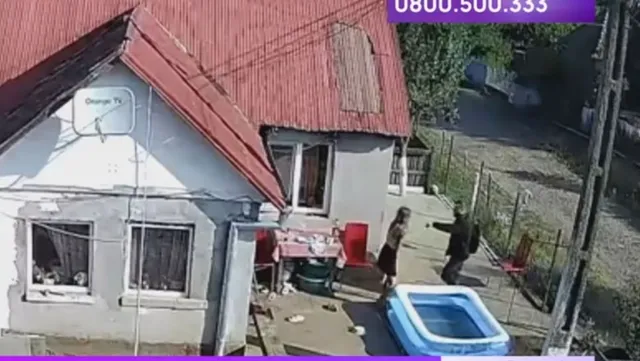 Biztonsági kamera felvétele egy udvarról: piros tetős ház előtt két személy áll, egy nő és egy férfi, közöttük feszült interakció látszik, a földön gyerekmedence és kerti bútor található.
