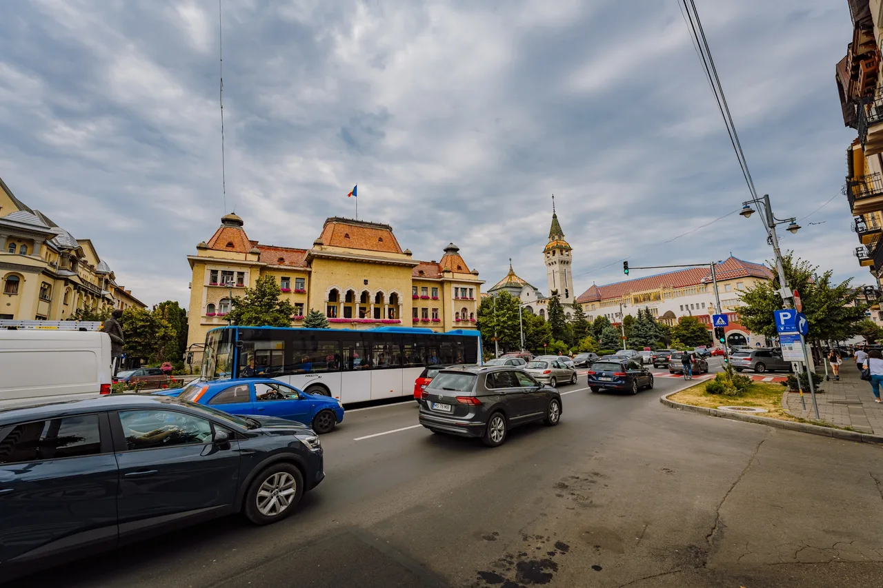 Forgalmas kereszteződés Marosvásárhely központjában, autókkal és busszal, háttérben a Prefektúra épülete és a Kultúrpalota tornya látható.