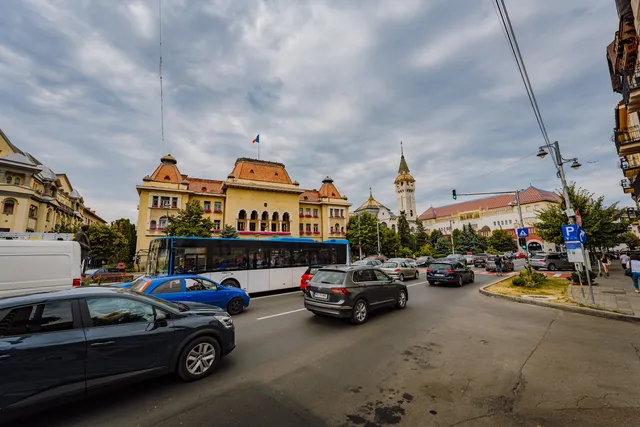Forgalmas kereszteződés Marosvásárhely központjában, autókkal és busszal, háttérben a Prefektúra épülete és a Kultúrpalota tornya látható.