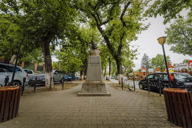 II. Rákóczi Ferenc mellszobra egy talapzaton, fák árnyékában, sétányon, mögötte parkoló autók és egy játszótér látható.
