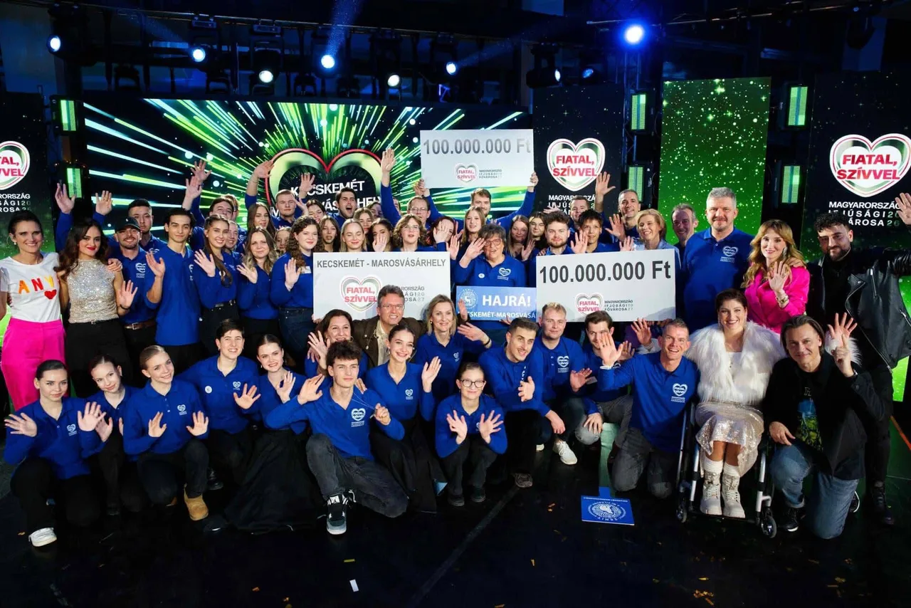 Nagy csoportkép egy televíziós stúdióban: kék pólós fiatalok és több felnőtt integetnek a kamerába, közöttük táblák „100.000.000 Ft” felirattal és „Kecskemét-Marosvásárhely” szöveggel, a háttérben „Fiatal, Szívvel” és „Magyarország Ifjúsági Fővárosa” feliratú kivetítők láthatók.