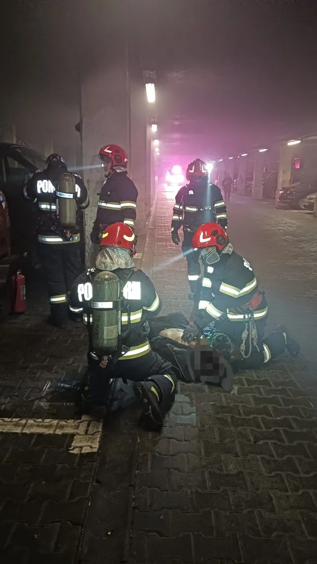 Éjszaka, füstös aluljáróban több tűzoltó gyűlik össze védőfelszerelésben, légzőkészülékkel; ketten a földön fekvő személy körül térdelnek, aki mellett ápolási eszközök láthatók.
