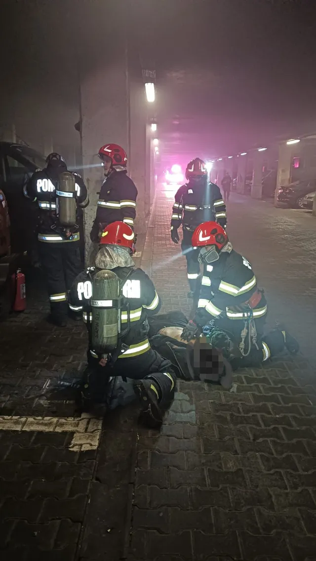 Éjszaka, füstös aluljáróban több tűzoltó gyűlik össze védőfelszerelésben, légzőkészülékkel; ketten a földön fekvő személy körül térdelnek, aki mellett ápolási eszközök láthatók.