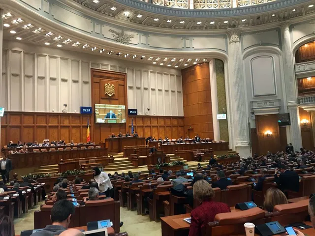 A román parlament plenáris ülésterme, díszes kupolával és oszlopokkal, tele képviselőkkel, elöl az elnökség asztala, felette kivetítő és óra látható.