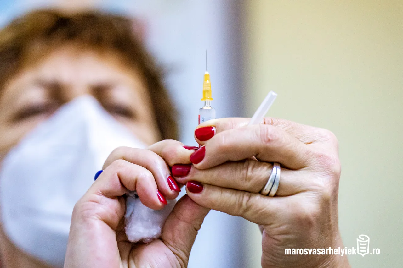 Orvosi maszkot viselő nő piros körömlakkal fest le egy ampullát, miközben egy fecskendő tűvel felszívásra előkészített injekció és egy vattacsomó látszik a kezében.