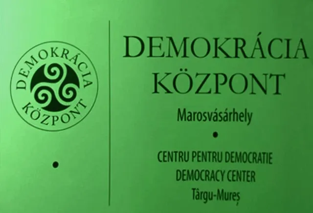 Zöld hátterű logó és felirat: 'Demokrácia Központ, Marosvásárhely' magyarul, románul és angolul, mellette egy kör alakú embléma spirál mintával.