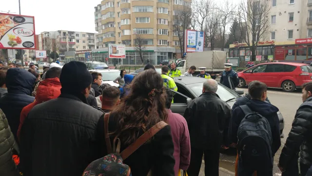 Utcán összegyűlt embercsoport figyel egy közlekedésrendőri intézkedést: két rendőr egy ezüst személygépkocsi mellett áll, a háttérben teherautó, autók és lakóépületek láthatók.