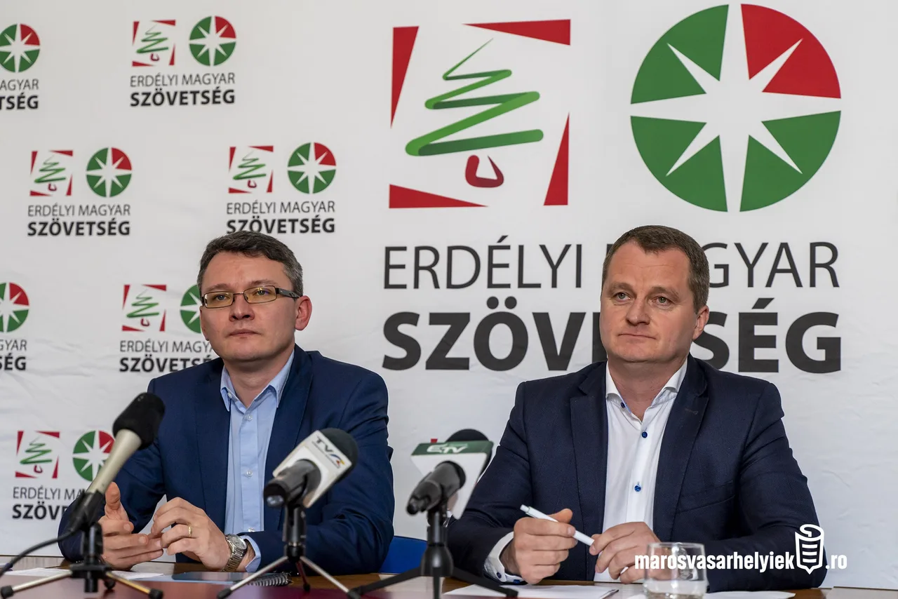 Két öltönyös férfi ül egy sajtótájékoztatón mikrofonok előtt, mögöttük az Erdélyi Magyar Szövetség logója és felirata látható a molinón.
