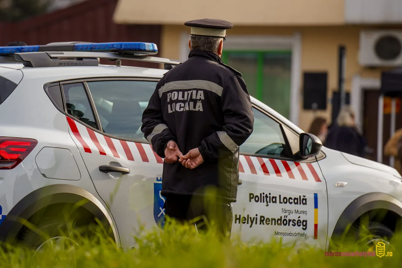 Marosvásárhelyi helyi rendőr sapkás egyenruhában, hátat fordítva, kezét háta mögött összefogva áll egy Politia Locala feliratú rendőrautó mellett.