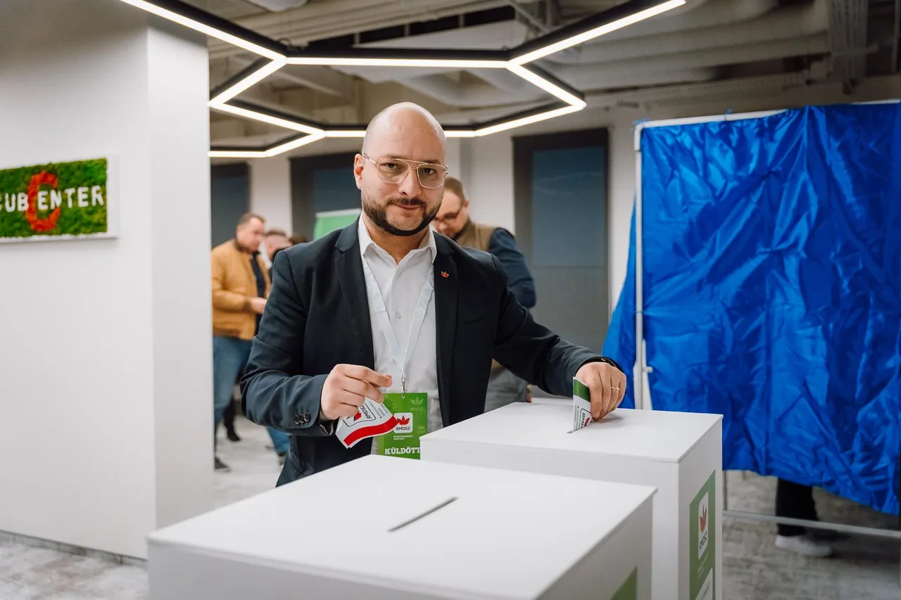 Öltönyt viselő, szemüveges férfi RMDSZ-jelvényes kitűzővel és „küldött” feliratú kártyával szavazólapot helyez egy fehér szavazóurnába, teremben, háttérben más emberek és egy kék elválasztófüggöny.