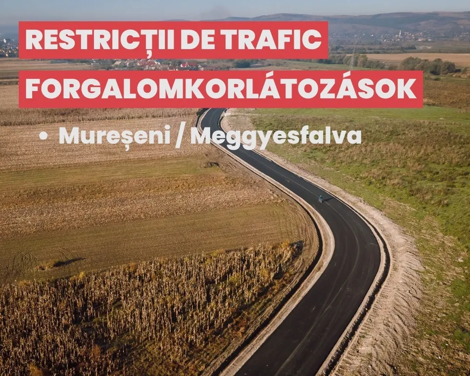 Légi felvétel egy kanyargós, frissen aszfaltozott útról mezők között, egy motorkerékpáros halad rajta; a képen felirat: „Restricții de trafic / Forgalomkorlátozások – Mureșeni / Meggyesfalva”.