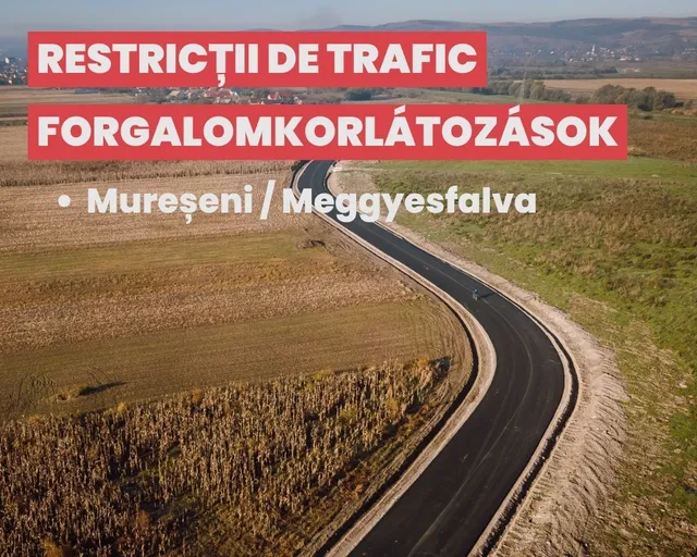 Légi felvétel egy kanyargós, frissen aszfaltozott útról mezők között, egy motorkerékpáros halad rajta; a képen felirat: „Restricții de trafic / Forgalomkorlátozások – Mureșeni / Meggyesfalva”.