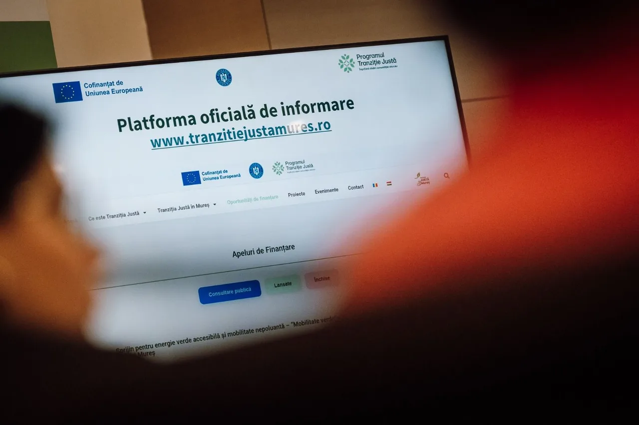 Számítógép-monitor képernyője, rajta a „Tranziție Justă Mureș” (Méltányos Átállás Program Maros megye) hivatalos tájékoztató weboldala látható, előtte homályosan egy személy keze és karja.