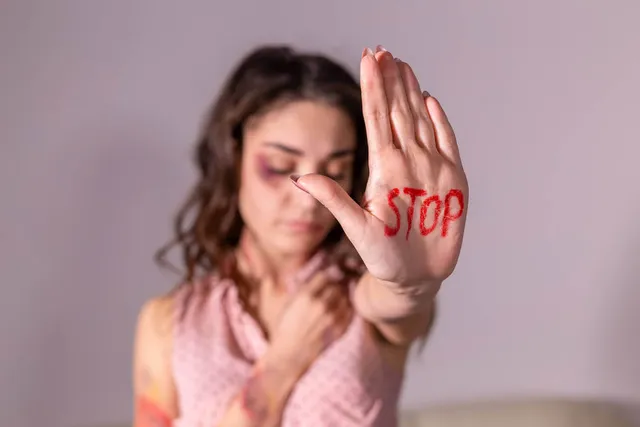 Fiatal nő tenyerét emeli a kamera felé, tenyerébe piros festékkel a „STOP” szó van írva; arcán kékfoltos, sérülésre utaló festés látszik, tekintete lefelé irányul.