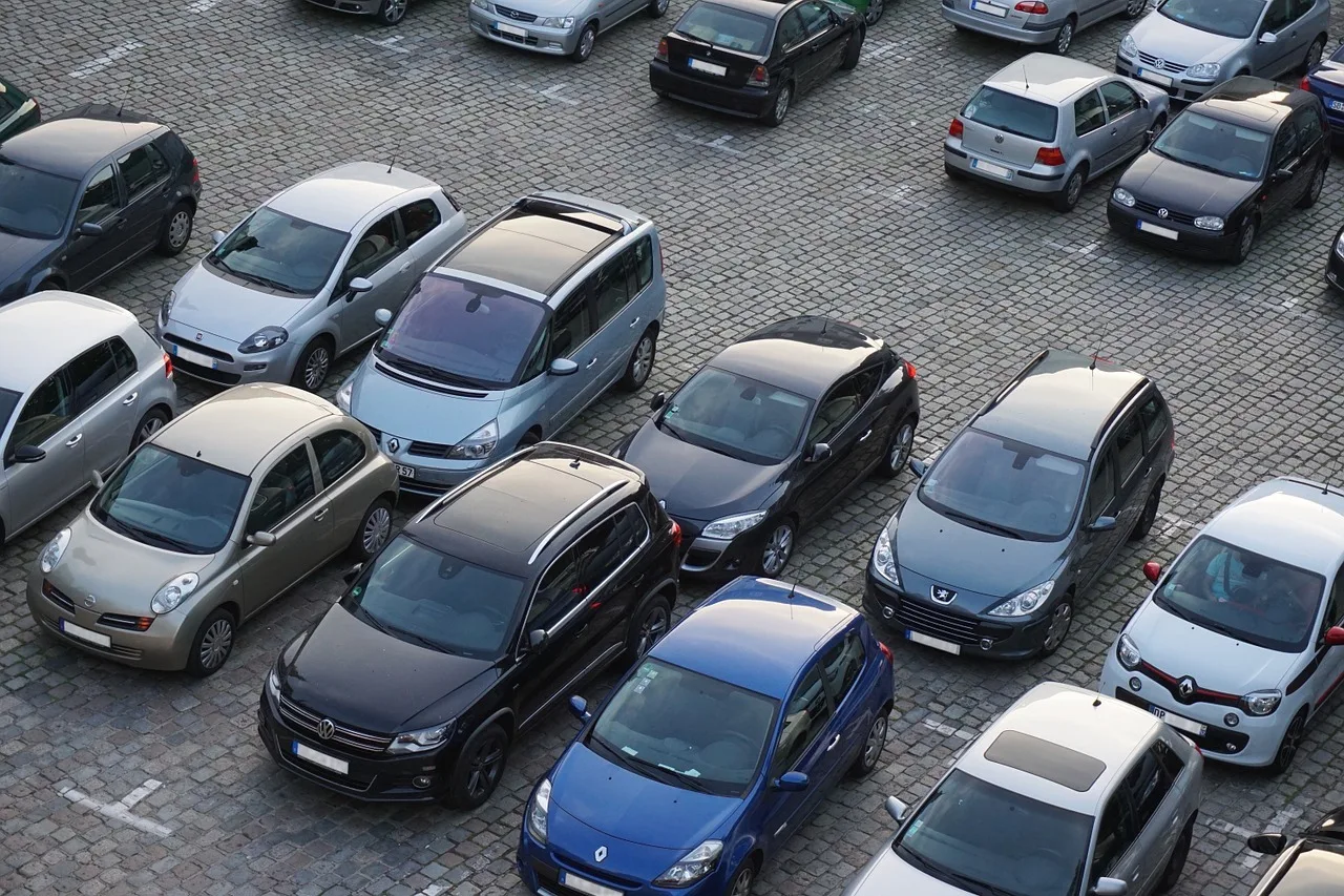 Madártávlatból fotózott kockaköves parkoló, ahol sűrűn egymás mellett parkolnak különböző színű és típusú személyautók.