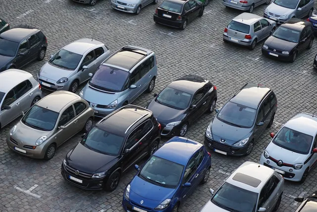 Madártávlatból fotózott kockaköves parkoló, ahol sűrűn egymás mellett parkolnak különböző színű és típusú személyautók.