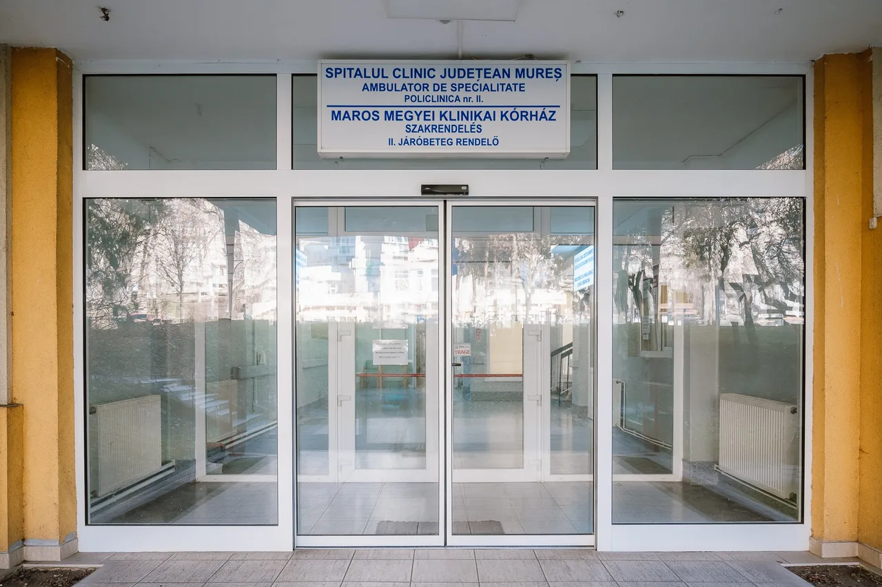 A Maros Megyei Klinikai Kórház 2-es számú járóbeteg-rendelőjének bejárata, üvegajtókkal, felette kétnyelvű (román-magyar) felirattal: „Spitalul Clinic Județean Mureș – Ambulator de Specialitate – Policlinica nr. II” / „Maros Megyei Klinikai Kórház – Szakrendelés – II. Járóbeteg rendelő”.