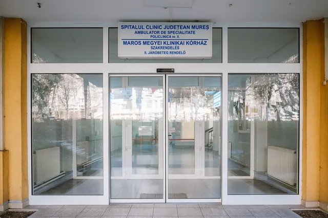 A Maros Megyei Klinikai Kórház 2-es számú járóbeteg-rendelőjének bejárata, üvegajtókkal, felette kétnyelvű (román-magyar) felirattal: „Spitalul Clinic Județean Mureș – Ambulator de Specialitate – Policlinica nr. II” / „Maros Megyei Klinikai Kórház – Szakrendelés – II. Járóbeteg rendelő”.