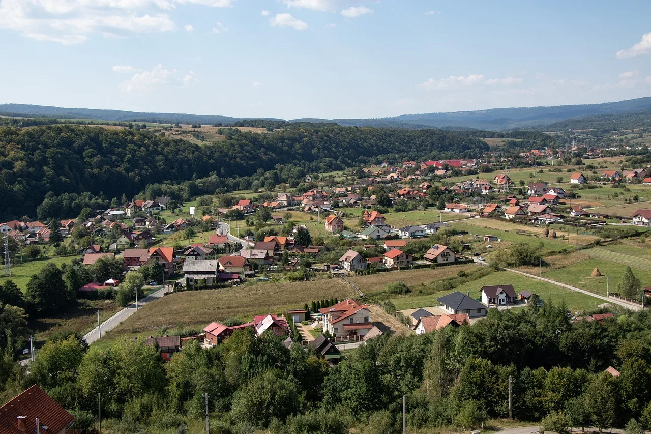 Madártávlati kép egy Maros megyei falu, kis településről völgyben, körülötte erdős dombokkal és hegyekkel. Piros és sötét tetős házak, kertek, rétek láthatók.