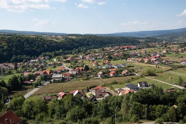 Madártávlati kép egy Maros megyei falu, kis településről völgyben, körülötte erdős dombokkal és hegyekkel. Piros és sötét tetős házak, kertek, rétek láthatók.