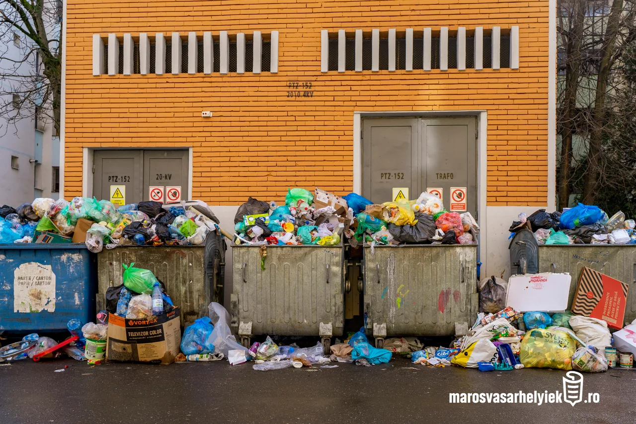 Túltelt szemétkonténerek sorakoznak egy narancssárga téglaépület előtt, a konténerek mellett és tetején szétszóródva műanyag zsákok, kartondobozok és egyéb hulladék halmozódik fel.