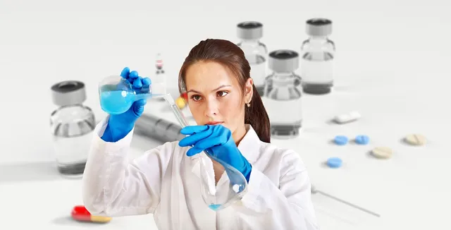 Fehér köpenyt és kék gumikesztyűt viselő nő laboratóriumi lombikból kék folyadékot tölt egy kémcsőbe, háttérben elmosódva injekciós üvegcsék és tabletták láthatók.