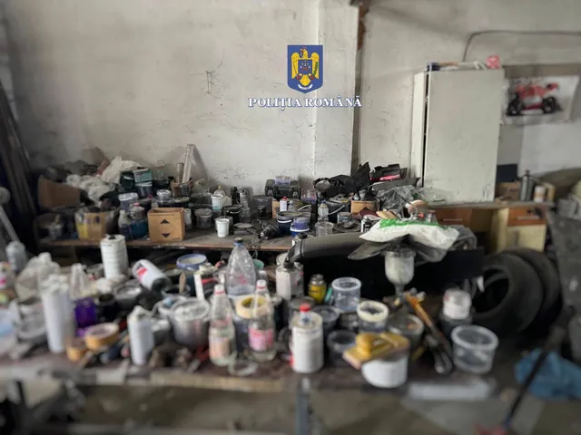 Egy garázs vagy raktár belseje, ahol asztalokon és a padlón nagy mennyiségű vegyi anyag, festékes dobozok, üvegek, kannák és egyéb tartályok halmozódnak fel rendezetlenül. A képen a Román Rendőrség (Poliția Română) logója szerepel vízjelként.