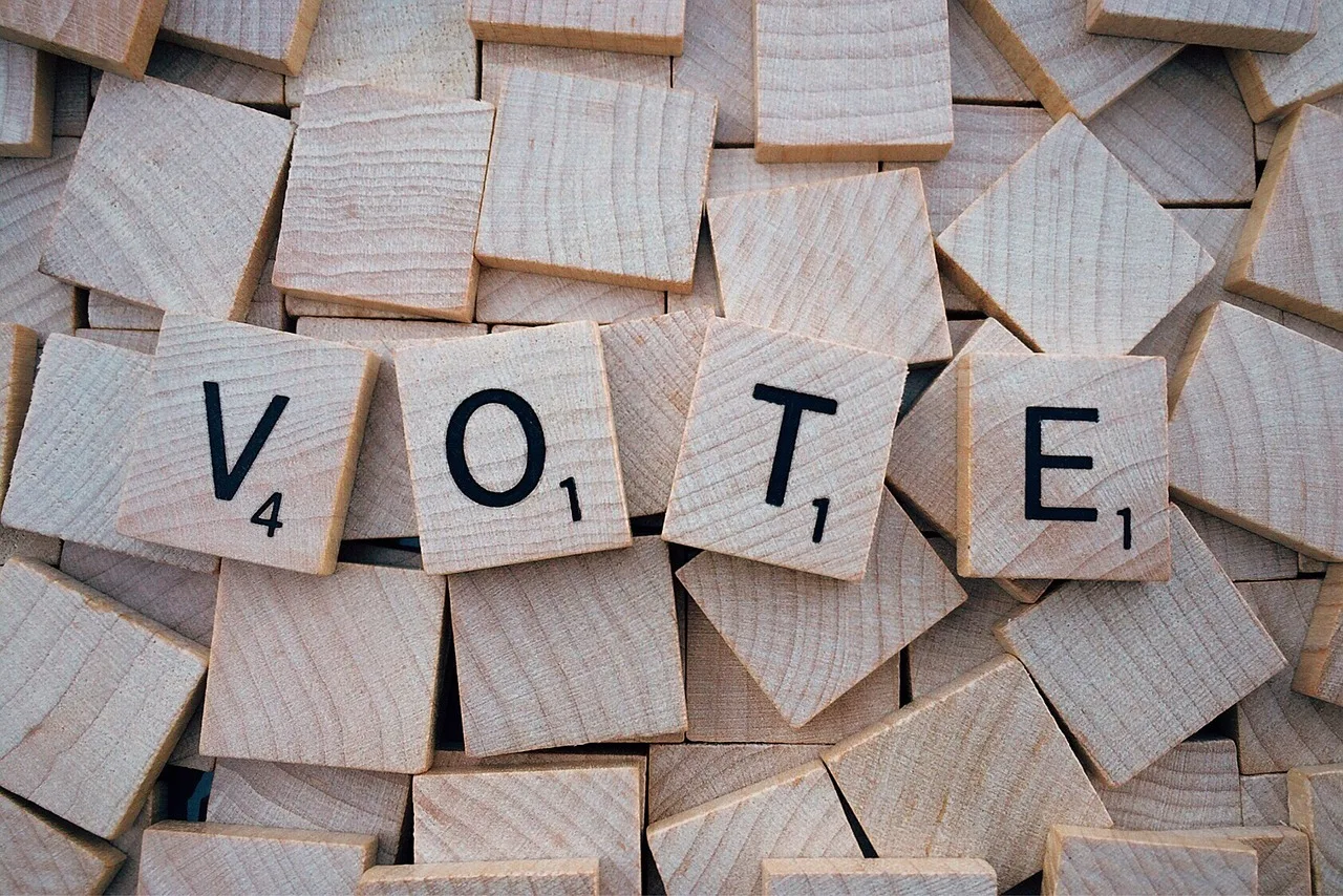 Üres fa scrabble-betűkockák halmaza, középen néhány kirakott kocka VOTE (szavazz) szót formál.