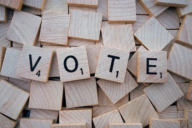 Üres fa scrabble-betűkockák halmaza, középen néhány kirakott kocka VOTE (szavazz) szót formál.